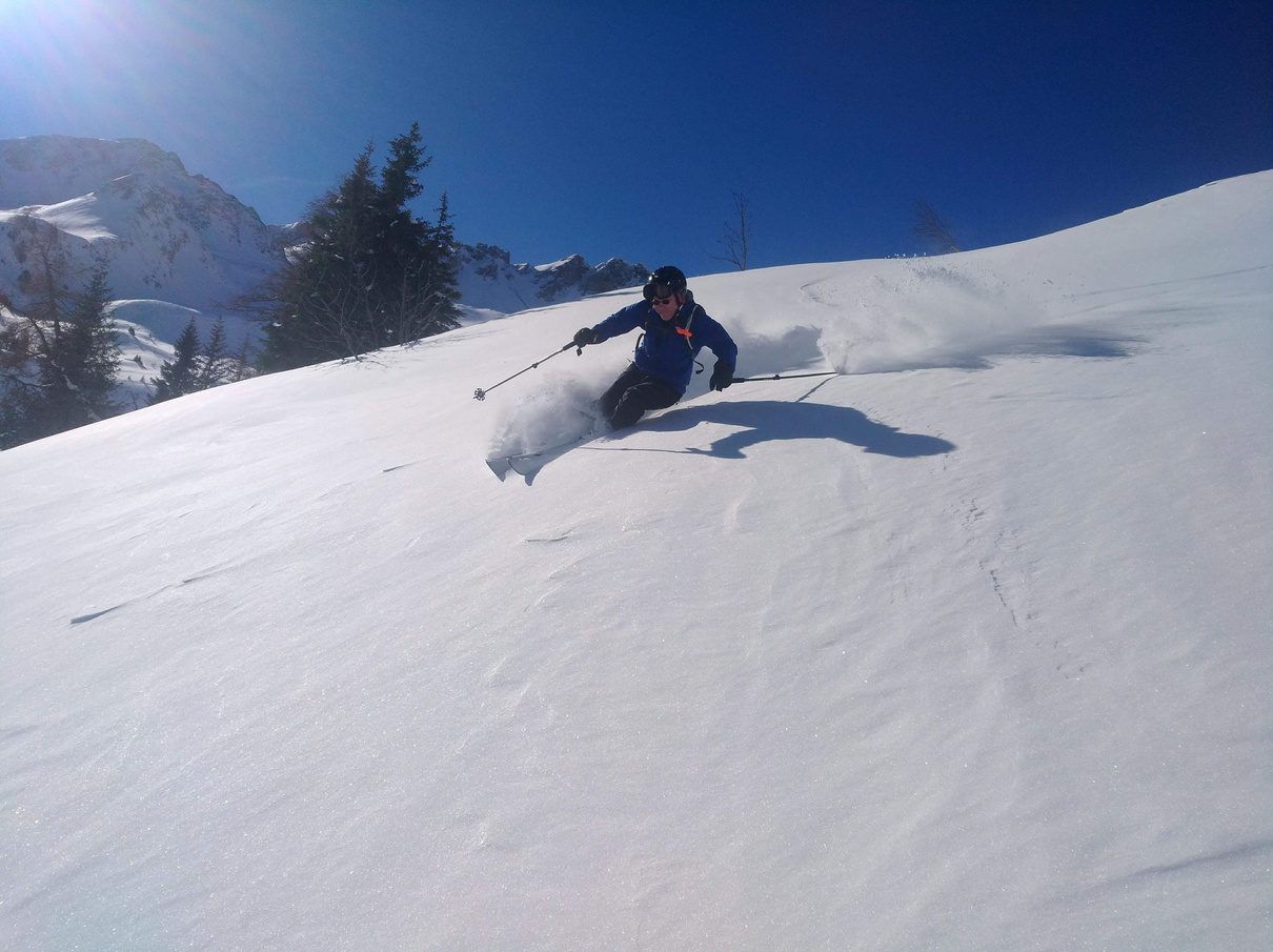Freerider zieht eine Spur durch unverspurten Tiefschnee unter Felswaenden