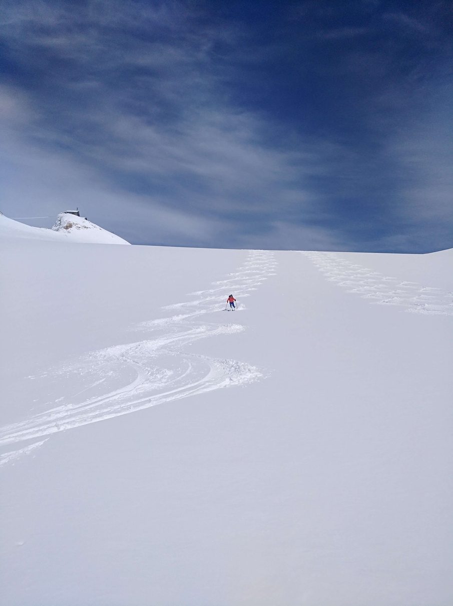 Einzelne Aufstiegsspur zieht ueber ein weites Schneefeld zu einer Huette