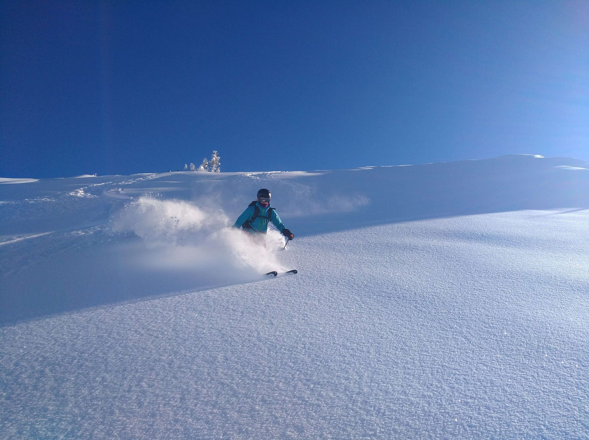 Skifahrer loest eine Puderschneewolke auf einem weiten Hang in Sportgastein aus